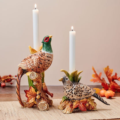 Two pheasant taper candleholders, a tall standing bird and a smaller ground bird, with lit white candles