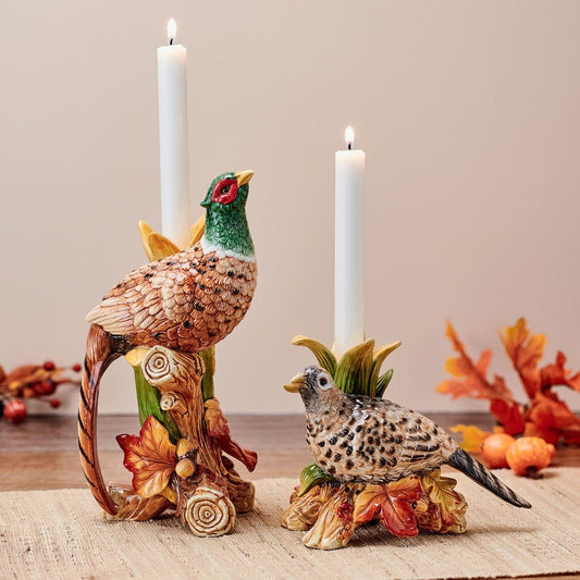 Two pheasant taper candleholders, a tall standing bird and a smaller ground bird, with lit white candles